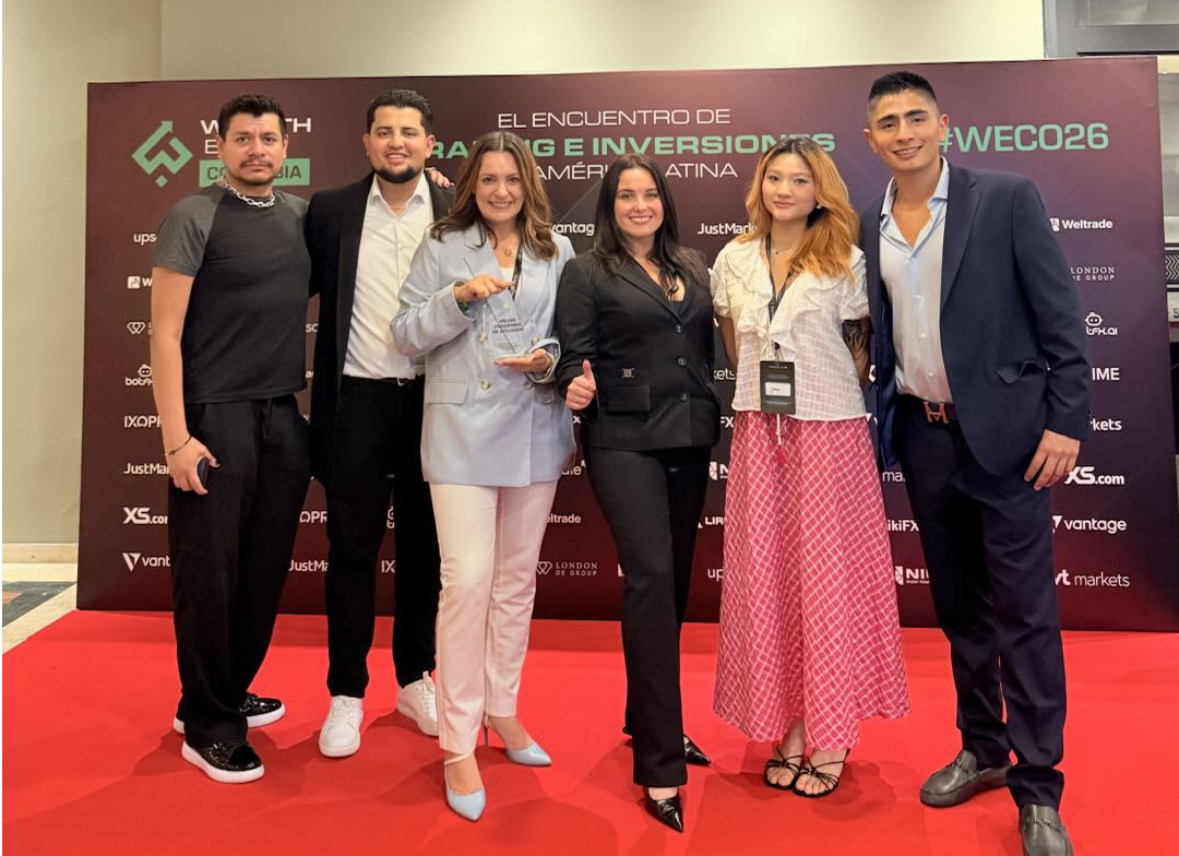 Group of seven professionals posing on a red carpet in front of a conference banner.